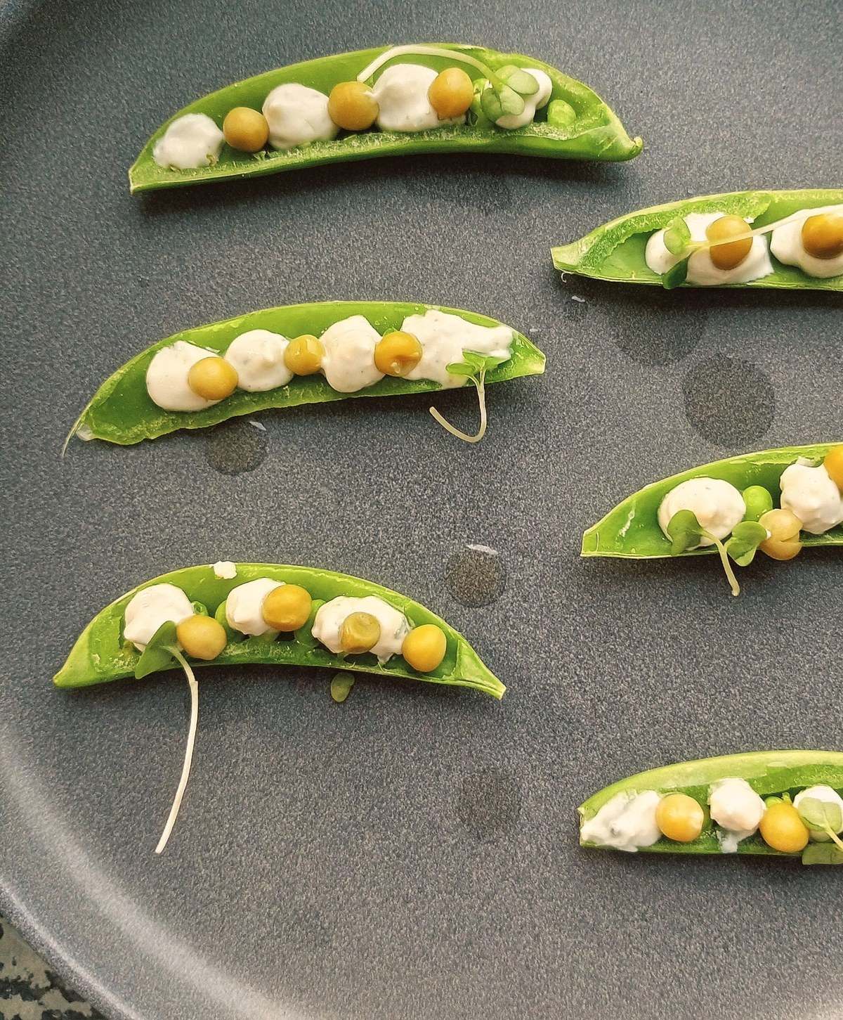 Cosses de petits pois garnies de petits pois et de crème, sur une assiette ardoise.