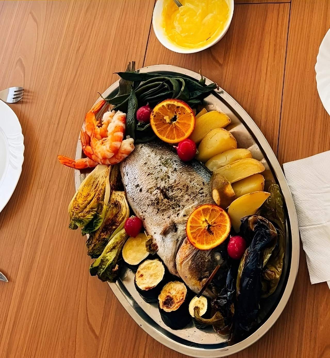 Plat à partager : poisson entier rôti, gambas, pommes de terre, légumes grillés et oranges.